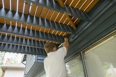 a man is painting the outside of a house with wood slats on it's roof