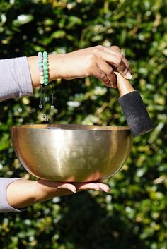 two hands holding a large metal bowl in front of some bushes with beads on it