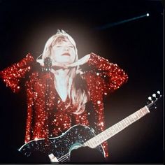 a woman with long hair holding a guitar in front of her face and wearing red sequins