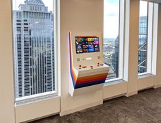 an arcade machine in the middle of a room with large windows looking out onto a city