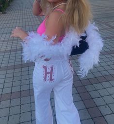 a woman in white pants and pink top with feathers on her arms, posing for the camera