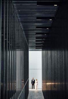 a man and woman are standing in the middle of a long hallway that is lined with metal slats