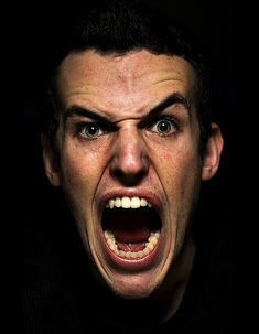 a man with his mouth open in the dark, making an angry face and looking at the camera