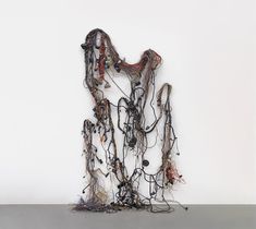 an abstract sculpture made out of wires and other objects on a table with a white wall in the background