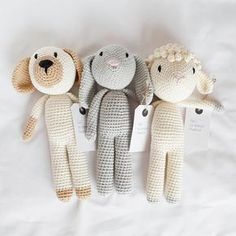 three crocheted stuffed animals sitting next to each other on a white sheet with tags