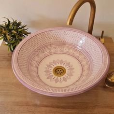 a pink and white bowl sitting on top of a wooden table next to a potted plant