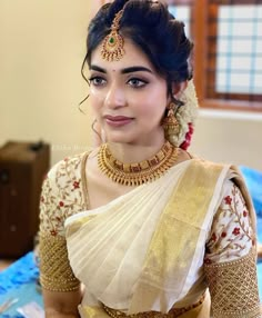 a woman in a white and gold sari with jewelry on her neck, posing for the camera