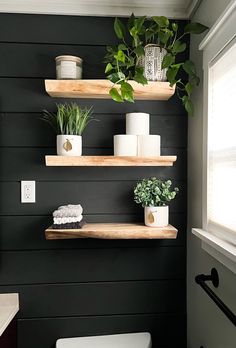 the bathroom is decorated in black and white with wood shelving, potted plants and toilet paper