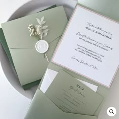 the wedding stationery is set on top of a white plate with a flower in it