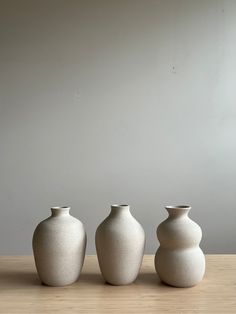 three white vases sitting on top of a wooden table