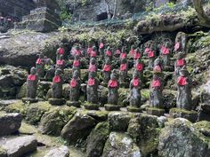 many statues with red ribbons on them in front of some mossy rocks and trees