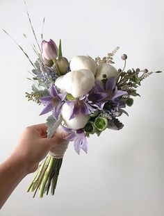 a hand holding a bouquet of flowers on a white background with purple and green accents