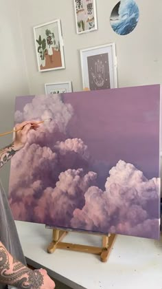 a man is painting clouds on an easel