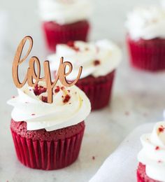 red velvet cupcakes with white frosting and one topped with a cake topper