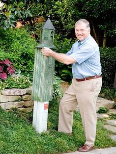 an older man standing next to a mailbox in the grass with his hands on it