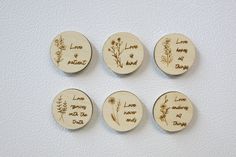 four wooden magnets with the words love and flowers engraved on them, sitting on a white surface