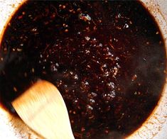 a wooden spoon in a pot filled with brown liquid and other things on the table