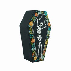 a black box with a skeleton on it and flowers around the edges is shown in front of a white background