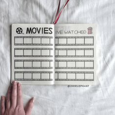 a hand is holding an open book with movies written on it and the film strip in front of them