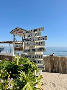 a sign that is on the side of a beach with flowers in front of it