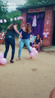 two women are dancing with pink balloons in front of them