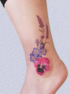 a flower tattoo on the foot of a woman's leg with purple and blue flowers