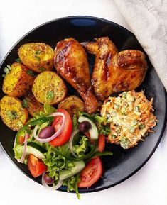 a black plate topped with meat and veggies on top of a white table