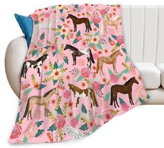 a pink blanket with horses on it sitting next to a white couch and pillows in the background