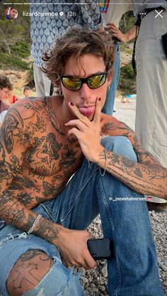 a man sitting on the ground with his tongue out and tattoos all over his body