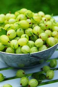 a metal bowl filled with green fruit sitting on top of a white table covered in leaves