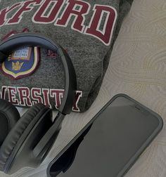 headphones, cell phone and sweatshirt on a bed with the university t - shirt