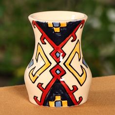 a colorful vase sitting on top of a table next to a green bush in the background