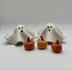 three ceramic pumpkins sitting next to each other in front of a white ghost's head