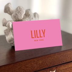 a pink business card sitting on top of a wooden desk next to a stuffed animal