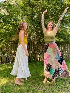 two women standing next to each other in the grass with their arms up and smiling