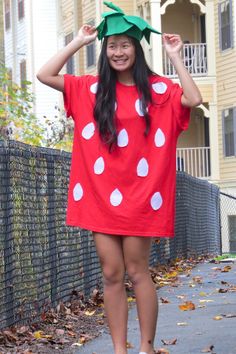 a woman in a red dress and green hat is standing on the sidewalk with her hands behind her head