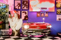 an old fashion car is parked in front of a purple wall with pictures on it