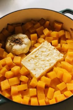 a pot filled with butter and cubed cheese next to a garlic onion on the side