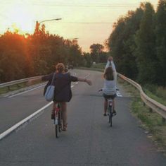 two people riding bikes down the road with their arms in the air as the sun sets