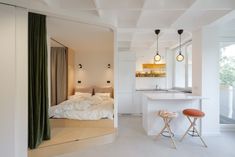 a bedroom with white walls and flooring next to a kitchen island in front of a bed