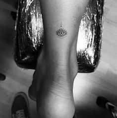 a woman's foot with an evil eye tattoo on the left side of her leg