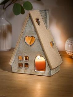 a small house shaped candle holder with a lit candle in the center on a wooden table