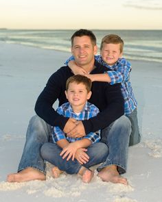 a man and two boys are sitting on the beach with their arms around each other