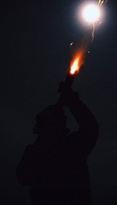 the silhouette of a person holding a flashlight up to their face in the night sky