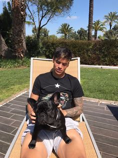 a man sitting in a lawn chair holding a small black dog with his legs crossed