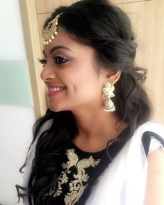 a woman in a black and white dress with gold jewelry on her head smiling at the camera