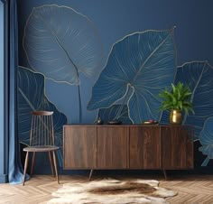 a living room with blue walls and large leaves on the wall behind a wooden cabinet