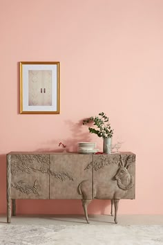 a pink room with a wooden sideboard and potted plant