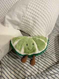 a green stuffed caterpillar sitting on top of a bed next to white pillows