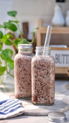 two jars filled with food sitting on top of a table next to a potted plant